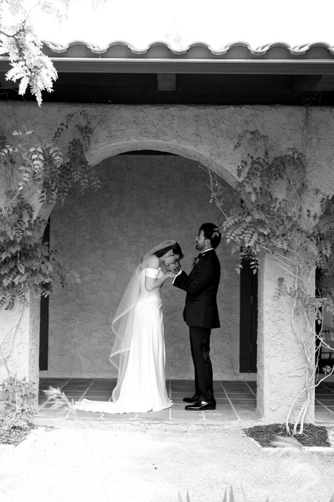 bride kissing groom's hand under the stucco archway at Villa Parker