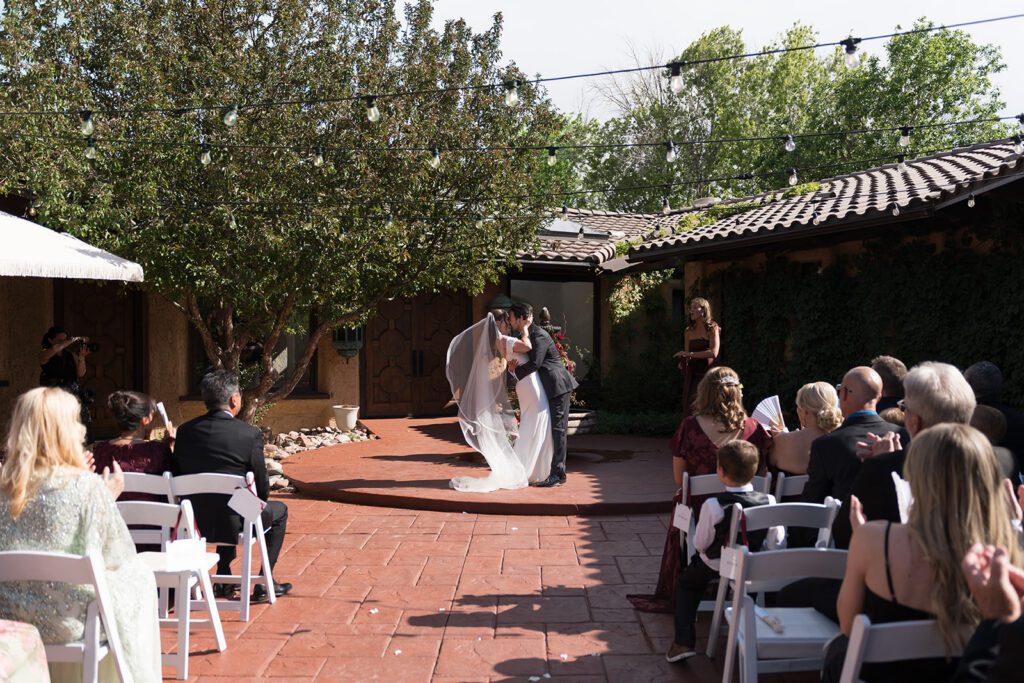 Wide view of a bride and groom's first kiss in the front courtyard at Villa Parker