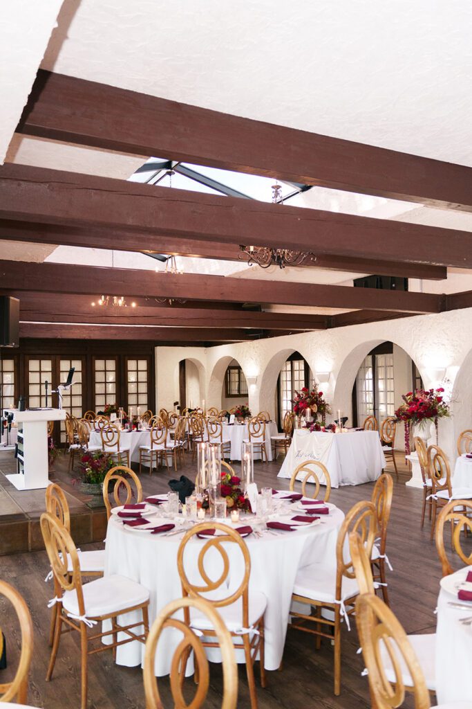 Reception tables set with red florals and burgundy napkins under the arches at Villa Parker