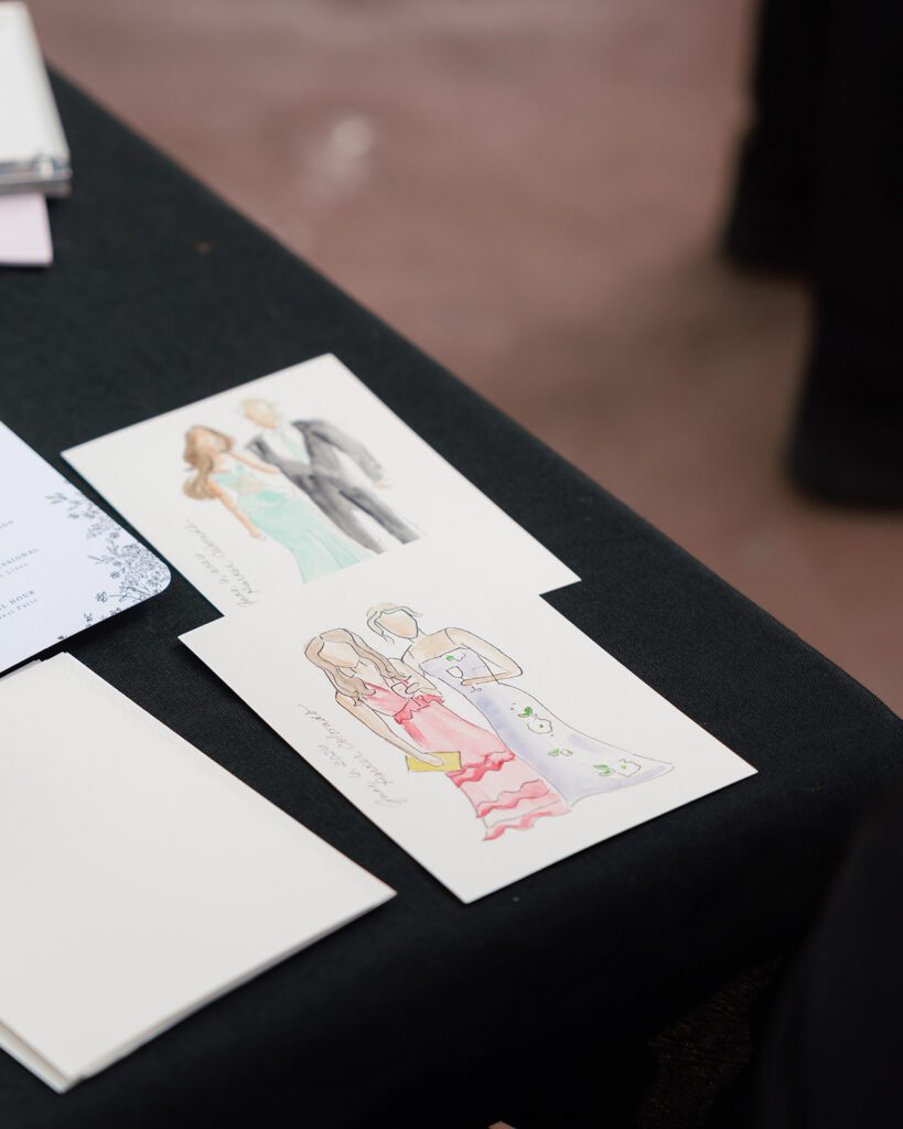 Finished watercolor portraits of wedding guests drying on a black tablecloth