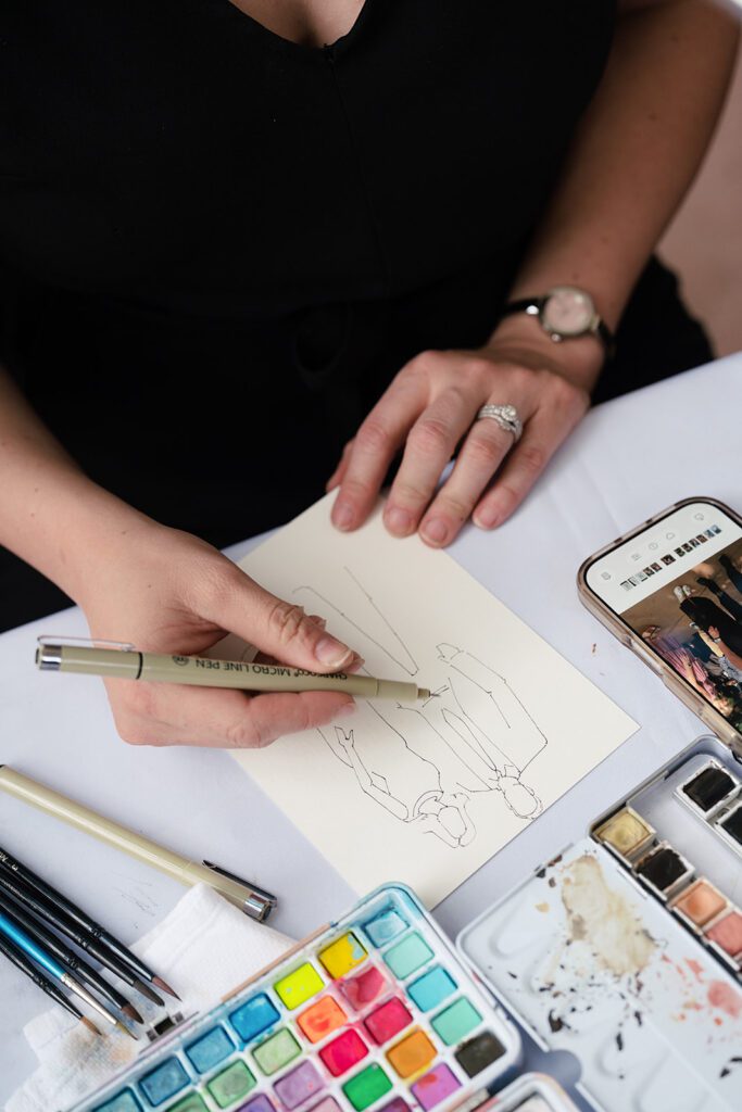 Live wedding painter sketching a guest portrait in ink beside a watercolor palette