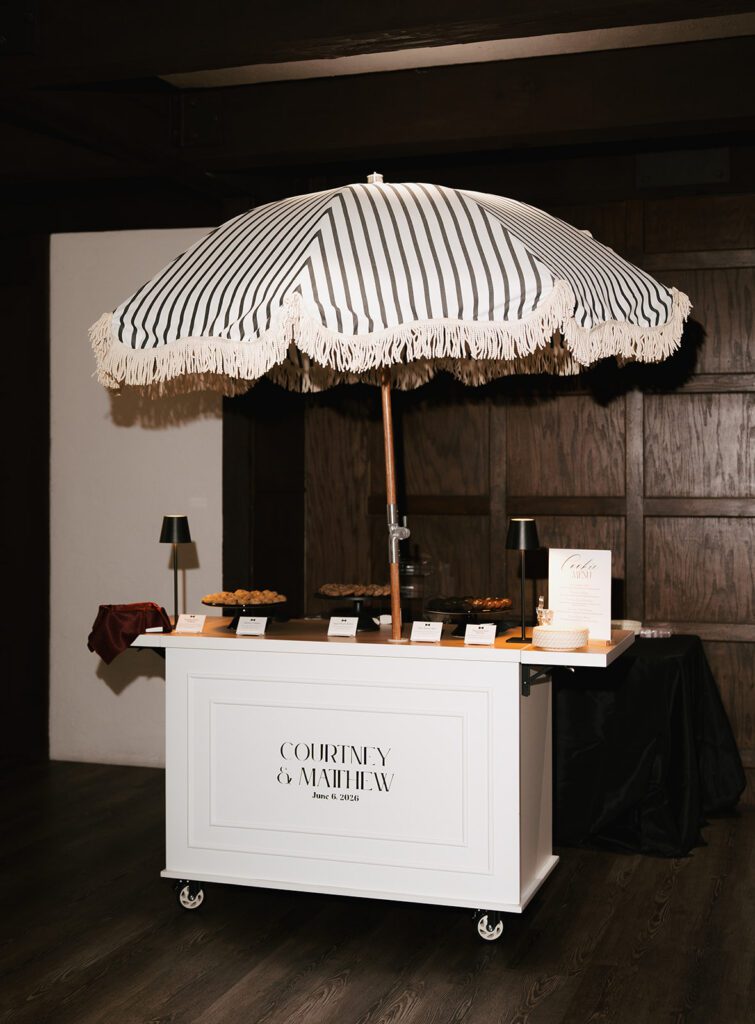 Custom cookie trolley under a striped fringed umbrella at the reception