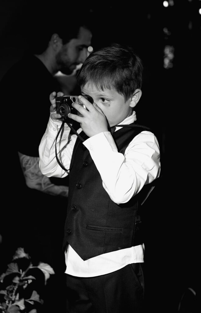 Young guest in a vest taking a photo on a film camera during the reception