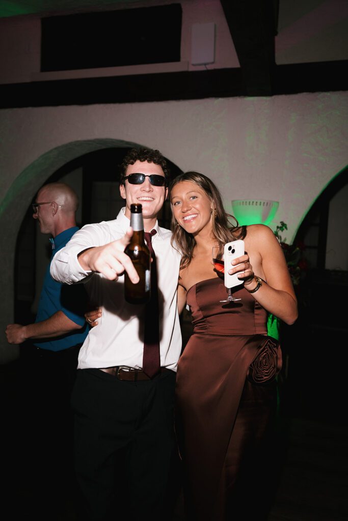 Guests laughing and dancing with drinks under green lights at the reception