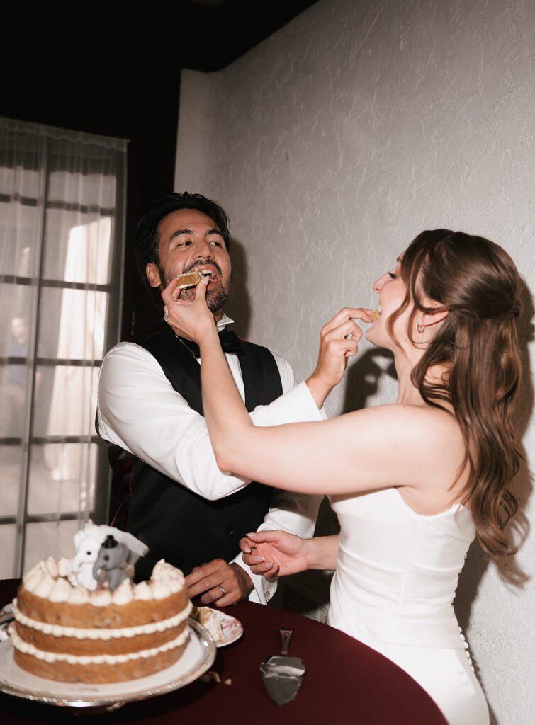 Bride and groom feeding each other cookie cake against a white stucco wall