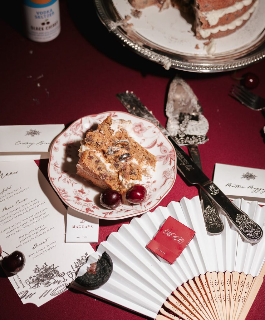 Slice of cookie cake with cherries, wedding rings, and a monogrammed red matchbook
