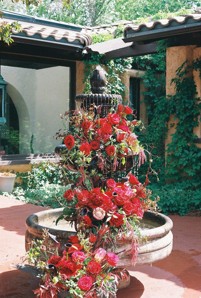 Stone fountain covered in red roses and amaranth at the Villa Parker entry courtyard
