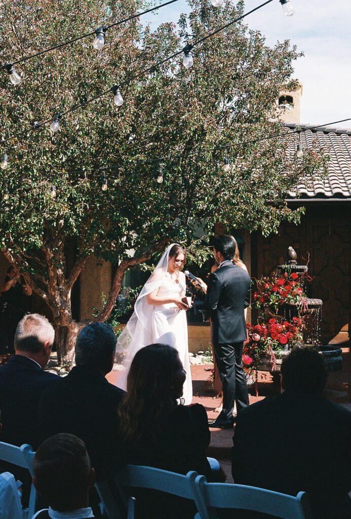 Bride and groom at the fountain altar surrounded by red florals during their Villa Parker ceremony