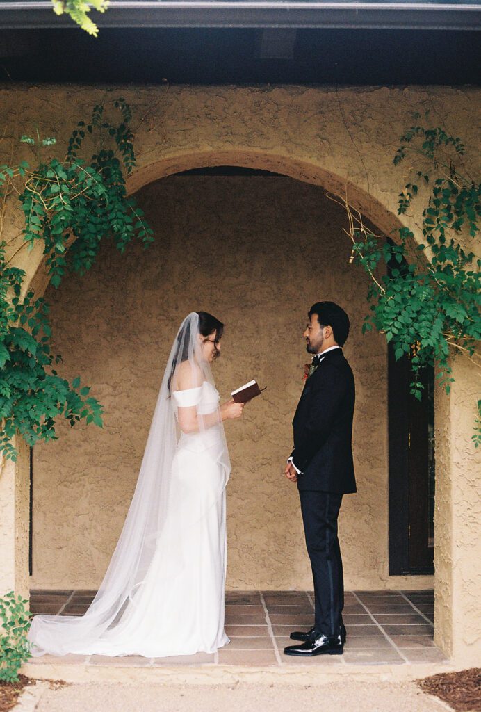 35mm film photo of Bride reading private vows from a leather book to her groom beneath a vine-covered arch at Villa Parker